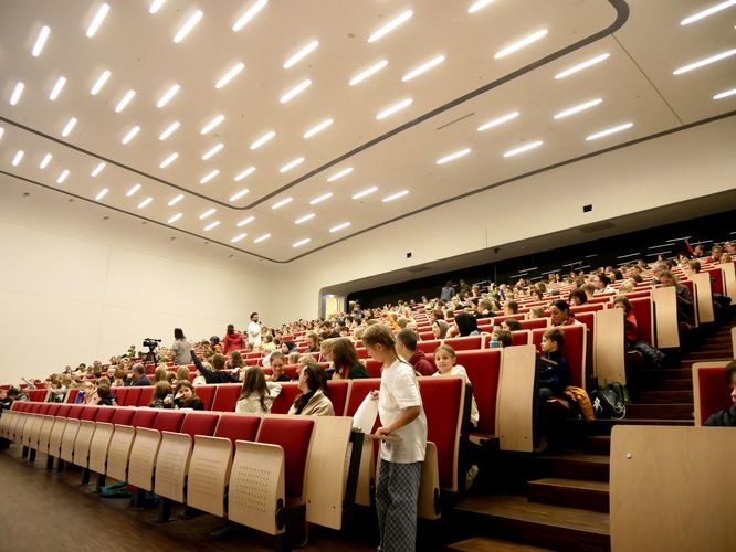 Blick in die Gesichter neugieriger Kinder sitzen in den Reihen eines sehr großen Hörsaals. 