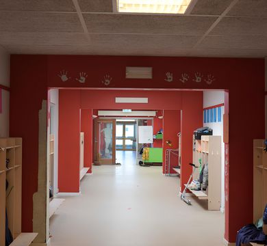 Das Bild zeigt den Gang einer Schule mit Garderoben und farbigen Wänden.