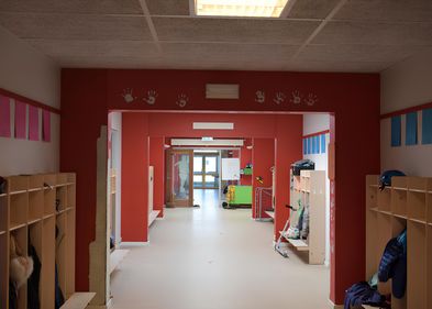 Das Bild zeigt den Gang einer Schule mit Garderoben und farbigen Wänden.