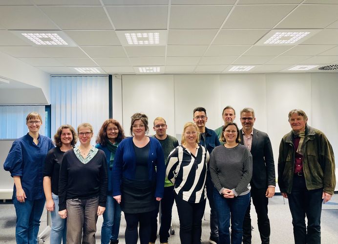 Das Foto zeigt insgesamt 12 Menschen, die nebeneinander stehen und gemeinsam in die Kamera lächeln. Sie sind Mitglieder eines Gremiums an der Universität Leipzig.